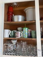 Cupboard shelf showing glasses, mugs, thermos, bucket, and pitcher.