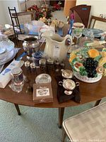 Wide view of table showing silver plate pitcher, salt and pepper shakers, butter shaper, and ceramic fruit cake holder on wood table.