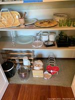 Shelves with vintage ceramic, glass, and kitchenware items including egg plate, floral plates, green glassware, ice buckets, wine rack, decanter, box of shells