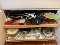 Two shelf drawers containing assorted pots, pans, baking trays, measuring cups, and lids.