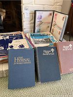 Photo showing hymnals 'The Hymnal for Worship & Celebration' and 'Hymns Family of God' in blue and maroon covers along with several vintage sheet music booklets and memorabilia folders.