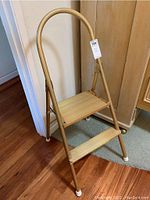 Full view of the metal step ladder showing its curved handle and two steps with rubber-capped feet.