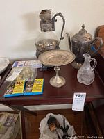 View of sterling silver coffee pot, glass pitcher, silver pedestal dish, and candles on a wooden table