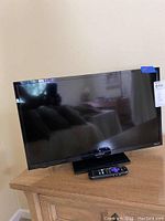 Photo of the 24 inch Sharp television on a wooden surface with remote control placed in front at the base of the TV