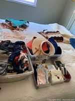 Overview of hats, scarves, and gloves on bed with two plastic storage bins