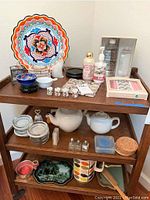 Full view of all items on wooden shelves: colorful ceramic plate, mini tea cup set, white teapots, coasters, candles, glass salt and pepper shakers, and decorative dishes.