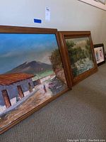 View showing two framed wall art paintings leaning against a wall, highlighting subjects and condition.