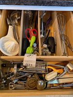 Drawer containing various metal, plastic, and wooden kitchen utensils including citrus juicers, scissors, graters, spoons, tongs, and whisks.