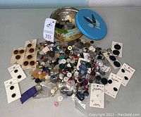 Photo showing the vintage Texas Fruitcake tin with lid off, surrounded by assorted buttons of various sizes, colors, and materials, some on cards and some loose.