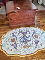 Cedar chest with visible wood grain and scratches on top surface with decorative oval rug partially underneath it