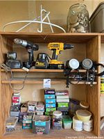 Wooden shelving unit with cordless power tools, two respirators, jars of wood knobs and various boxes of nails and screws on shelves.