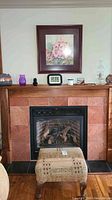 Full view of footstool in front of fireplace with floral painting hanging above it
