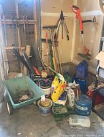 Whole garage corner showing assorted garden tools, gas cans, wheelbarrow, and soil bags