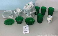 Overview of green glassware including plates, bowls, glasses, and the ceramic cup, some items wrapped in tissue paper for protection.
