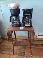 Metal drop leaf table with two coffee makers placed on top, showing front view