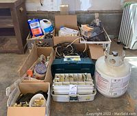Overview photo showing four boxes, two crates, a green toolbox open with hardware compartments visible, and a propane tank placed on the floor.