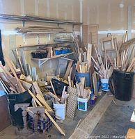 Garage/workshop with assorted wood pieces piled and stored in bins, buckets and leaning against walls. Includes planks, lattice panels, turned wood parts and various sizes of wood pieces.