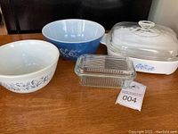 Photo showing all items together on a wooden table: three Pyrex mixing bowls in different sizes, CorningWare covered casserole, and covered glass butter dish.