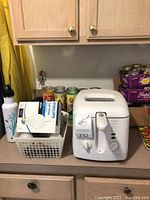 Rival deep fryer on kitchen counter with canning jars and Philips box in basket, water bottle and canned goods in background