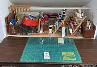 View of sewing supplies on table including wooden thread spool racks with many thread spools, scissors, glue bottles, and rotary mat