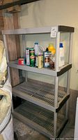 Full view of gray plastic storage shelf holding cleaning supplies and garbage can.