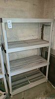 Full view of the plastic storage shelf with three slatted shelves against a concrete wall.