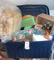 Photo of blue 40-gallon plastic storage tub filled with foam pieces, stuffing in plastic bags, floral fabric, and some wooden upholstery tools and materials.