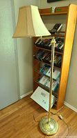 Brass floor lamp next to oak media stand with several VHS tapes and Nintendo Wii box below.