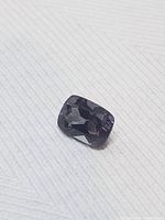 Cushion-cut natural alexandrite gemstone on white textured fabric, showing deep purple color under ambient light.