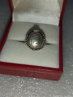 Closed top-down view of round domed lid with engraved leaf motif and beaded trim