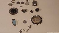 Full view of assortment of vintage sterling silver jewelry items including rings with black and blue stones, pendants, charms, and earrings on a textured white surface.