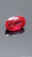 Close-up of oval loose ruby gemstone on a dark surface showing its facet cuts and red color.
