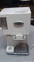 Front-facing image of the white Cuisinart ice cream maker showing the device in full with visible drip tray and logo.