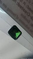 Rectangular green emerald on reflective surface with text background
