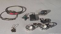 Assorted sterling silver and gold rings, earrings, and bracelets arranged on a woven fabric background.