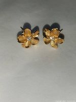 Photo of two 14K gold Hawaiian flower stud earrings each with a diamond in the center against a neutral background.