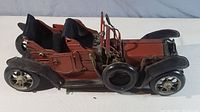 Side view of the hand-made metal model car showing brownish-red body, black leather seats, and black fenders.