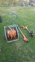 Full lot showing hose reel with orange hose, blue sprinkler hose, and two weed eaters on grass.