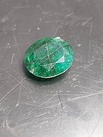 Close-up of natural emerald gemstone showing inclusions and scratches on a dark surface.