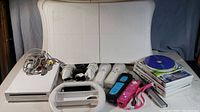 Nintendo Wii system components including console, AV cables, four Wii Remotes, two Nunchuks, two balance boards, steering wheels, and games.