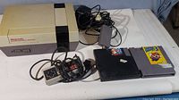 Photo showing the original Nintendo Entertainment System console, two wired controllers, power adapter, and two game cartridges including Super Mario Bros. 3.
