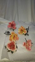 Five handmade pewter and porcelain rose flowers displayed on foam with visible repaired broken petals.