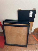 Four black IKEA Ribba frames stacked showing profile and front glass each approximately 22 inches square