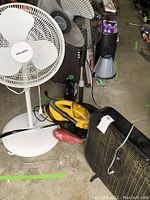 White Peconis fan, black Holmes oscillating fan, yellow Eureka handheld vacuum, black Holmes box fan, and Conair blow dryer arranged on concrete floor with some dust and dirt, cords visible.