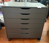 Front view of grey IKEA Alex cabinet with all six drawers closed and on casters, showing overall condition and structure.