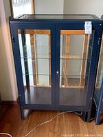 Full front view of dark blue Ikea Fabrikor cabinet showing both glass doors, frame, shelves and key in lock.