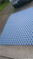 Full view of the blue and white outdoor polypropylene rug laid out on concrete showing overall size and pattern.