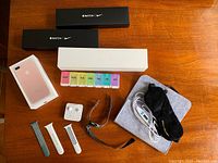 Photo of entire lot on wooden surface including empty Apple Watch Nike and standard boxes, iPhone box, Apple EarPods, pill organizer, Apple Watch bands, USB heated eye mask in case, and Timex watch.