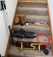 Full view of the items displayed on carpeted stairs including skateboard, snowshoes, baseball bats, gloves, balls, ski poles and flying disc.