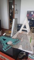 Two white distressed metal letter 'A's standing upright and two teal distressed wooden letter 'A's on a table with corrugated metal pieces